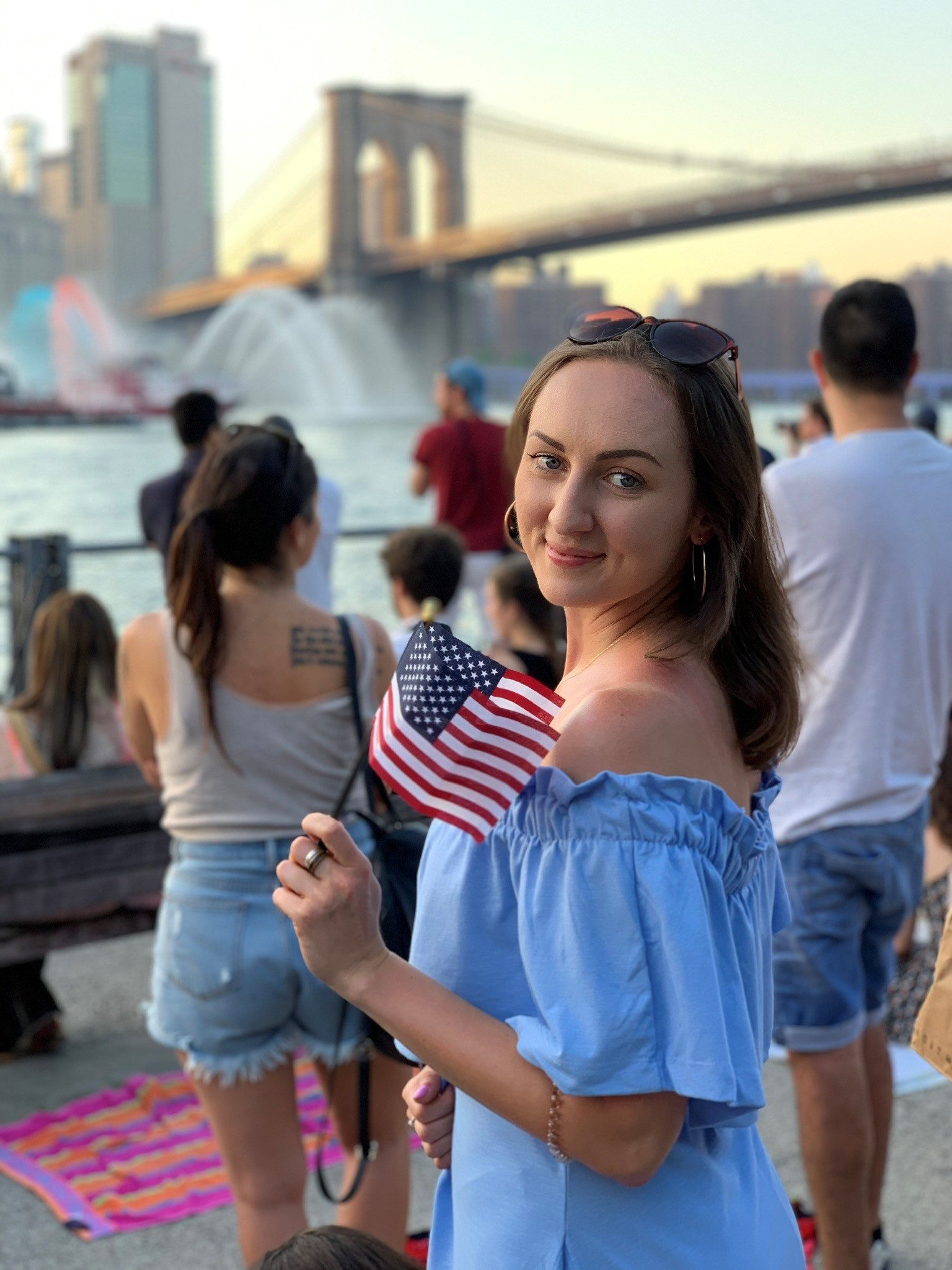 Joven con una bandera de Estados Unidos frente al puente de Brooklyn