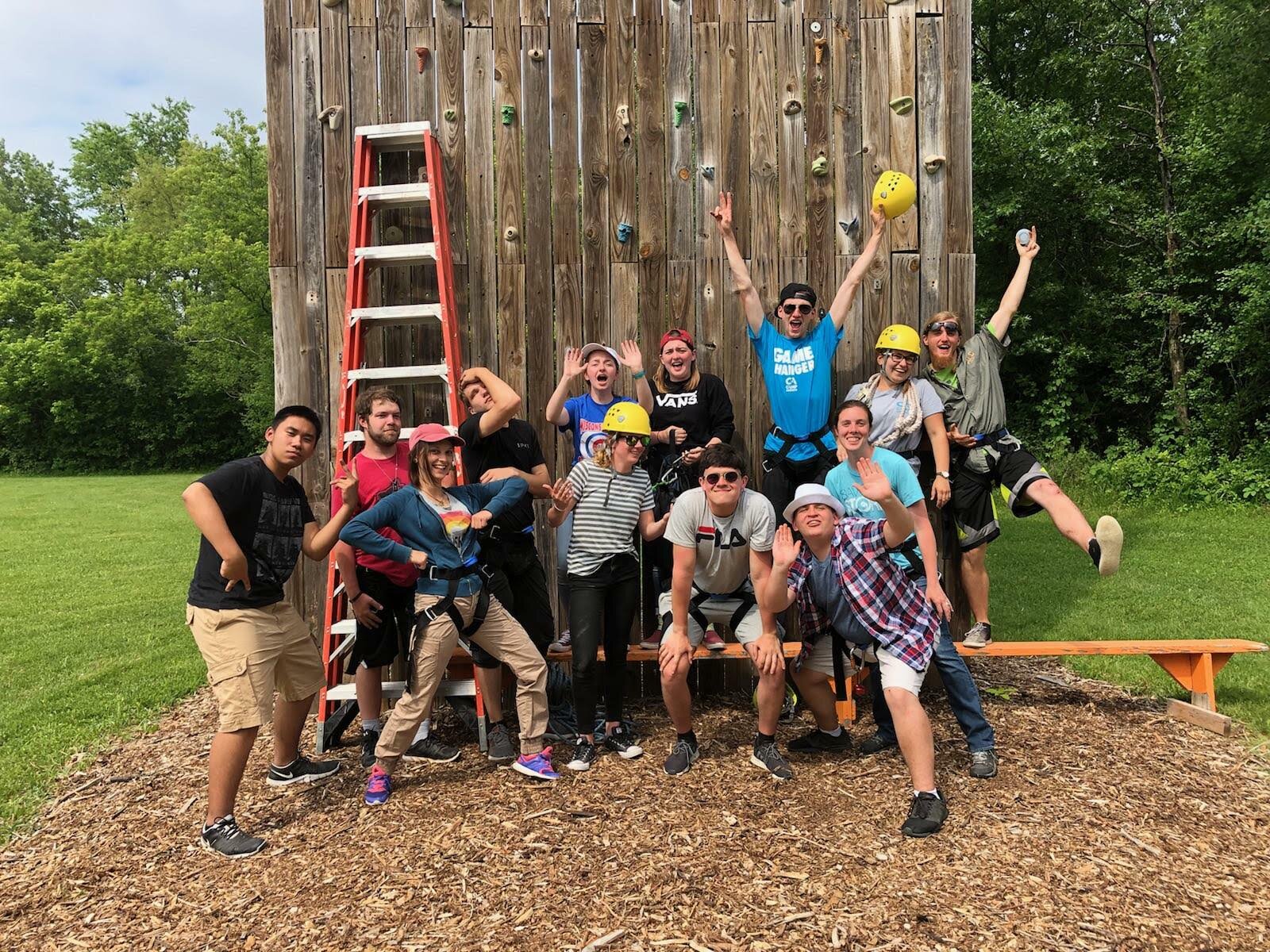 Grupo de participantes junto a un muro de escalada en un campamento